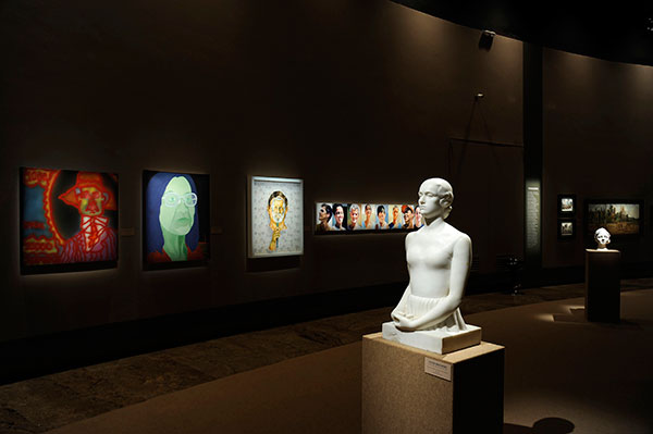 sala de exposição escura com escultura em primeiro plano e quadros ao fundo